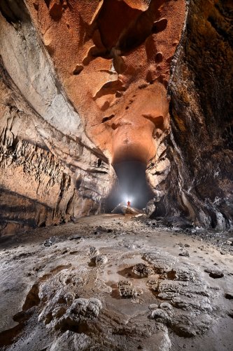 Cueva Fresca (Cantabrie, Espagne) - Grande galerie au plafond orange avec personnage en fond perché sur un rocher (cadrage large avec plafond).(SP-26-0940 )